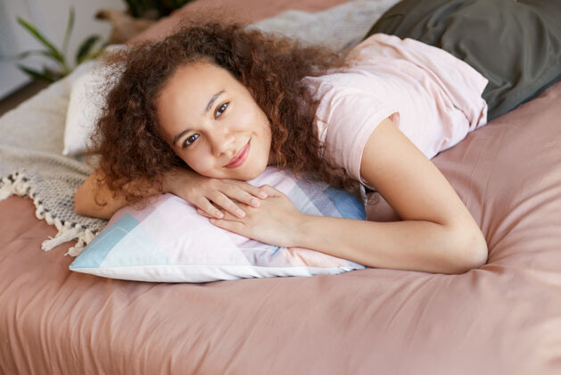 休息年轻的美籍黑人可爱的卷发女士躺在床上 看起来很开心 在家里享受阳光和微笑周末女性积极