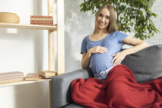 笑脸微笑着坐在沙发上抱着肚子的孕妇女商人妈妈水平