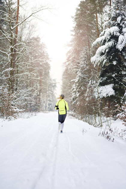 后方在冬天森林里奔跑的女人的后视图运动员健活方式专业