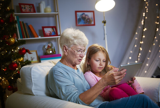 深情与祖母和科技共度圣诞节坐着晚上女孩