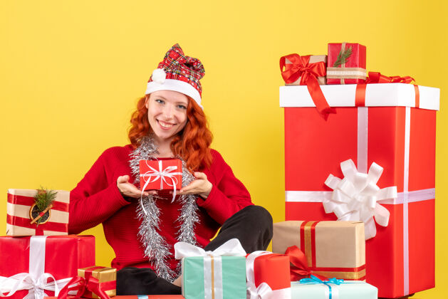礼物坐在黄色墙上的圣诞礼物周围的年轻女子的正视图礼物圣诞节年轻女性