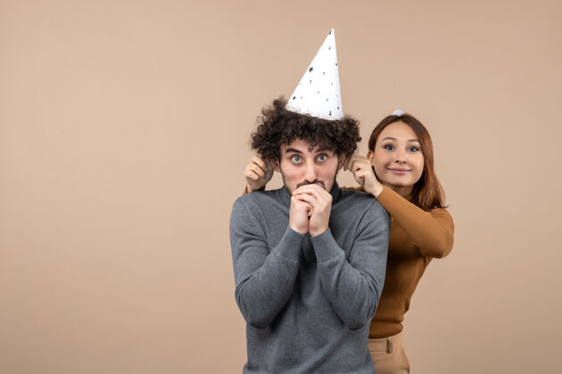 年轻的情侣可爱兴奋的年轻夫妇戴着新年帽微笑的女孩站在男孩后面 拉着灰色的耳朵可爱男人帽子