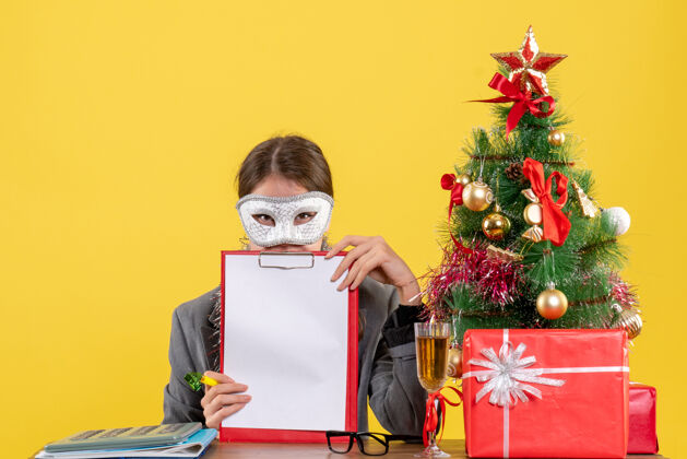 礼物正面图：戴着化装面具的年轻女孩坐在桌子旁 手持圣诞树和鸡尾酒文件女孩桌子
