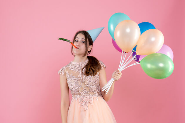 乐趣好奇的派对女孩 戴着派对帽 拿着气球 在粉色上用隔音器女孩聚会生日