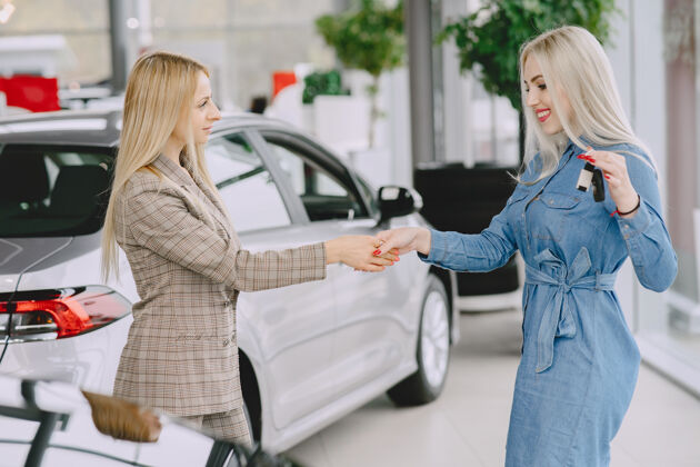 购买汽车沙龙里的女士买车的女士穿着蓝色裙子的优雅女士经理给客户钥匙车辆顾客汽车