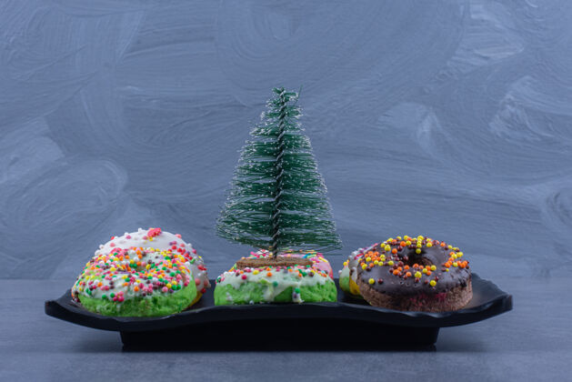 好吃一个黑色的盘子里有美味的甜甜圈和小圣诞树好吃深色盘子