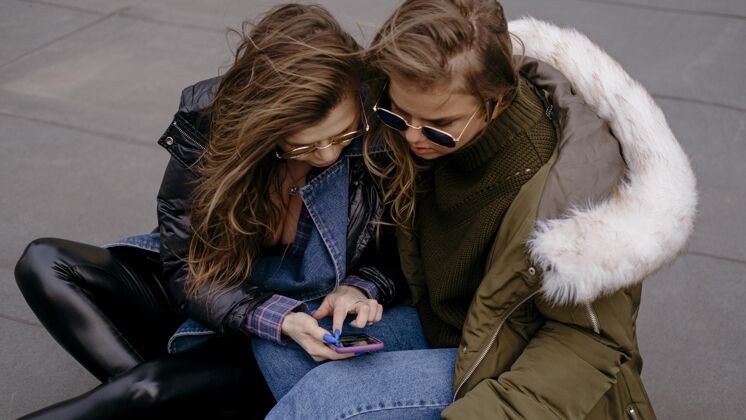 休闲女性朋友一起玩智能手机户外横向消遣女性