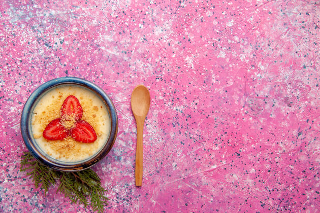 顶部顶视图美味奶油甜点 淡粉色桌面上有红色草莓片甜点冰淇淋甜水果浆果木制勺子餐具草莓