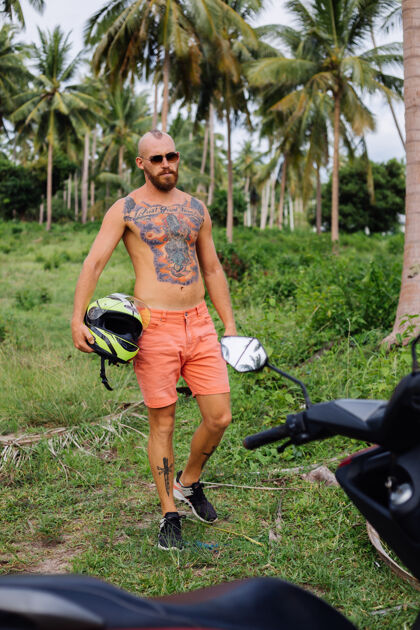 手在热带丛林的田野上纹着红色摩托车的壮汉自然自由夏天