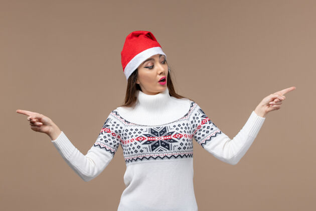 女士正面图棕色背景上戴着红色圣诞帽的年轻女子圣诞新年感慨模特新棕色