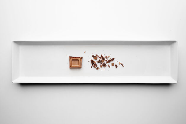 食物巧克力方块和碎料隔离在白色桌子背景的中心矩形陶瓷板上块小吃苦