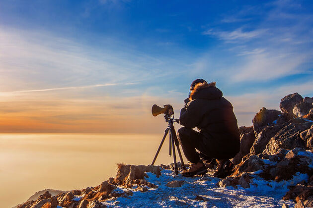 日出专业摄影师用相机在落日岩石峰上的三脚架上拍照暗色调日落摄影师雾