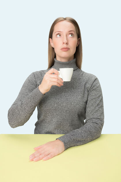 严肃美丽孤独的女人坐在蓝色的工作室里 手里拿着一杯咖啡 看起来很悲伤悲伤女人年轻