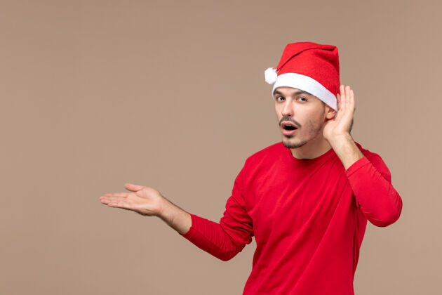 一正面图：年轻的男性在一个棕色背景的圣诞假期里仔细聆听密切背景微笑