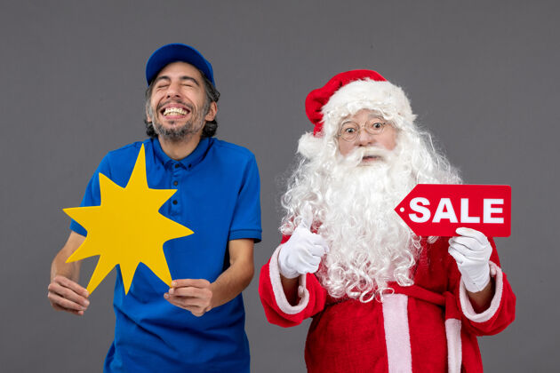 销售圣诞老人的正面图 男性信使手持销售横幅 灰色墙上有黄色标志庆祝圣诞快乐人