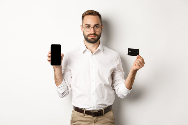 付款严肃的商务人士展示手机屏幕和信用卡网上购物的概念成人手势商人