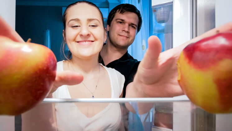 素食主义者一对饥肠辘辘的夫妇晚上从厨房的冰箱里拿出食物的画像节食和健康营养的概念食物餐具门
