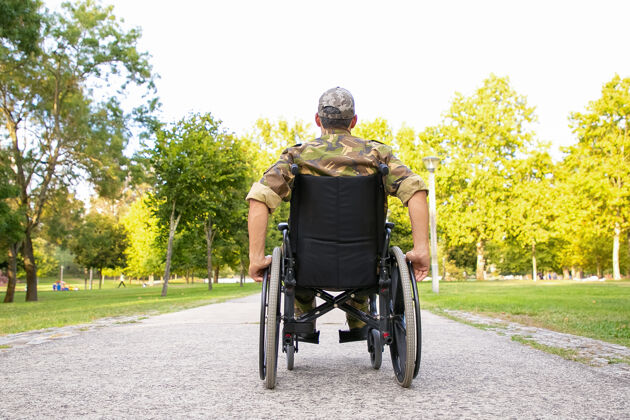 残障一个残疾的退休军人坐着轮椅在城市公园的人行道上走后视图战争或残疾的退伍军人的概念轮子成人椅子