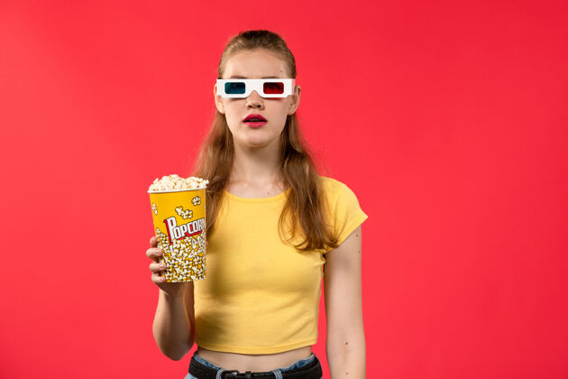 年轻女性正面图年轻女性在电影院拿着爆米花包戴着d太阳镜在红墙电影院看女性趣味电影漂亮电影院电影