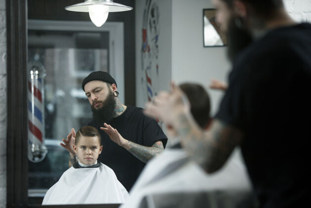 男儿童理发师在黑暗中剪小男孩儿子工作理发店