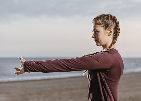 锻炼在海滩边伸展运动的女人的侧视图户外健身水平
