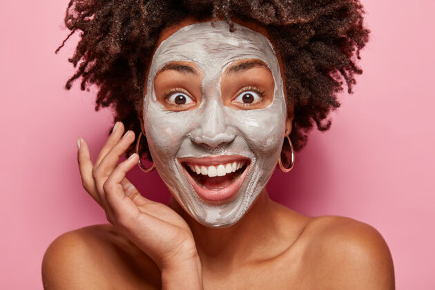 身体快乐的美国黑人女士的特写肖像脸上有白色的泥质面膜 笑容灿烂 美容手术后惊讶有新鲜的皮肤 有美容师或美容师的咨询放松清洁乐观