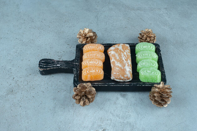 甜点饼干包装和果冻糖果在一个小托盘中松果在大理石表面甜点曲奇美味