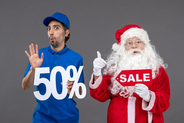 帽子圣诞老人的正面图 男性快递员持有50%的股份 灰色墙上挂着销售横幅圣诞快乐圣诞老人十二月
