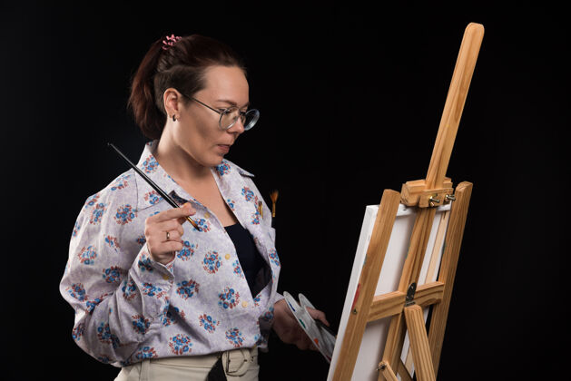 艺术品女画家拿着画笔 看着黑色背景上的画布艺术家艺术画笔