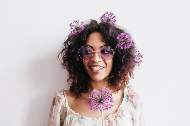 休闲幸福的黑发女孩戴着时髦的眼镜 头发上摆着鲜花卷曲的非洲女人站着紫色的葱花束休息模特