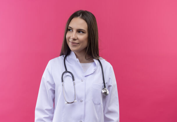 医生看着身边穿着听诊器医用长袍的年轻医生女孩 背景是孤立的粉色侧边年轻粉色