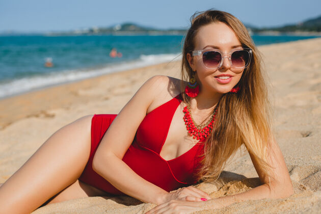 夏天年轻漂亮的金发女人穿着红色泳衣 戴着墨镜在沙滩上晒太阳性感时尚太阳