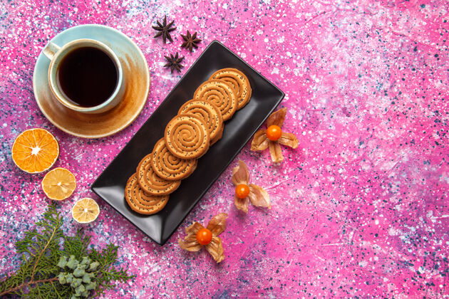 茶在浅粉色的表面上有一杯茶的黑色形状里面的甜饼干的俯视图饮料生的里面