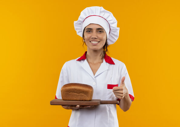 穿面带微笑的年轻女厨师穿着厨师制服拿着面包就用拇指向上切着复印空间厨师面包拿