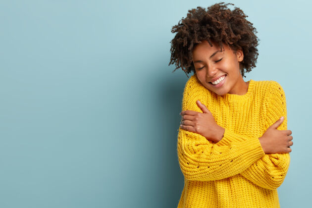 舒适快乐的年轻黑皮肤女人拥抱自己 感觉温暖舒适 穿着黄色针织毛衣满足跳跃清爽