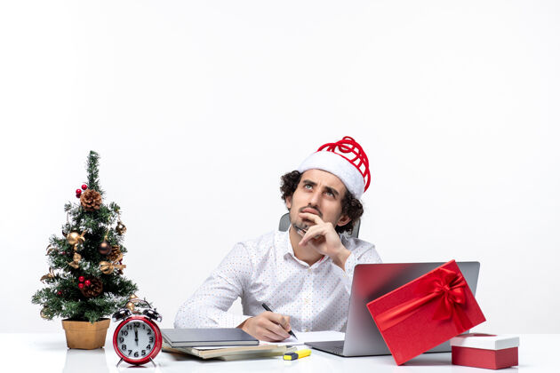 成年人专注的年轻商人 戴着有趣的圣诞老人帽 在白色背景的办公室里检查书写笔记 俯瞰并庆祝圣诞节写作看检查