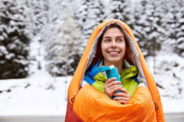 季节微笑的女游客在雪山上徒步旅行 在睡袋里取暖 喝热茶或咖啡饮料高山温暖