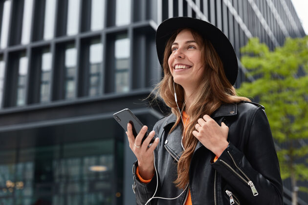 耳机迷人梦幻女子照片在大都市户外散步时手持现代手机 听音乐聊天心情手机