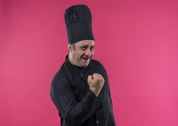 男性身着厨师制服的快乐中年男厨师在隔离的粉色墙壁上显示“是”的手势 并留有复印空间展示中年快乐