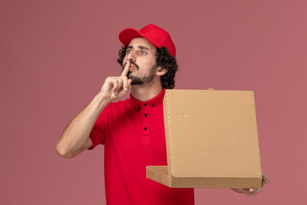 红色正面图：身穿红色衬衫和披风的男性快递员手持浅粉色墙上的送货食品箱肖像粉色食物