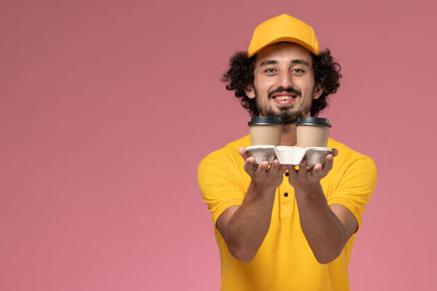 快递员正面图：身穿黄色制服 披风的男性快递员手持咖啡杯 粉色墙上挂着微笑咖啡黄色制服
