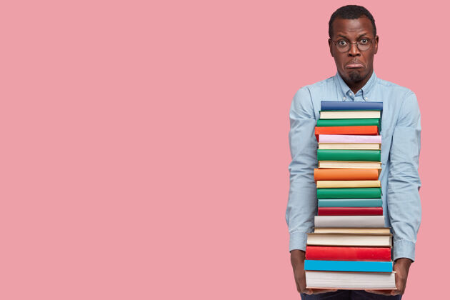 图书馆不满意的黑人青年拿着一堆课本 不满意地学习 噘着嘴 穿着正式的衣服空白堆衣服