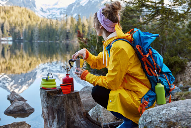 饮料年轻女子的户外景观用旅游设备煮咖啡 树桩上有便携式煤气炉茶工具徒步旅行
