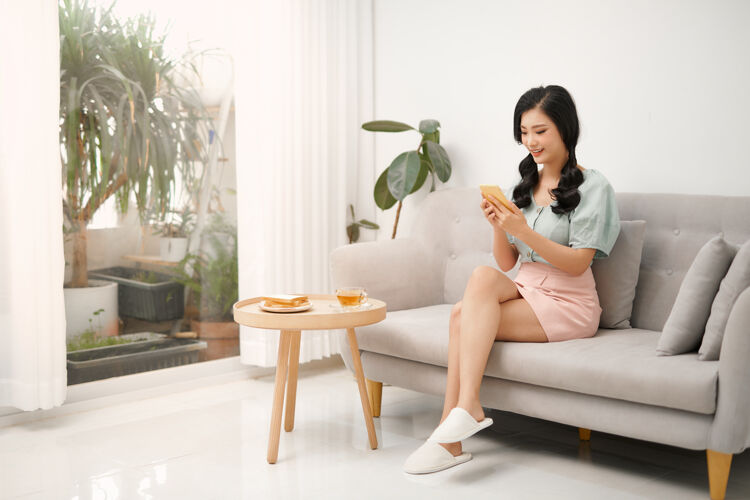 中文年轻女子坐在沙发上用智能手机聊天互联网漂亮亚洲