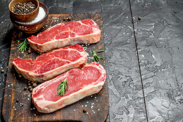 肉在一张黑色的乡村桌子上放着盐和香料的生大理石牛肉牛排生的大理石香料