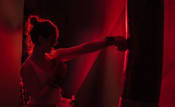 锻炼轮廓女拳击手拳击手套打拳在黑暗的背景下红色霓虹灯打拳袋女孩健身女人