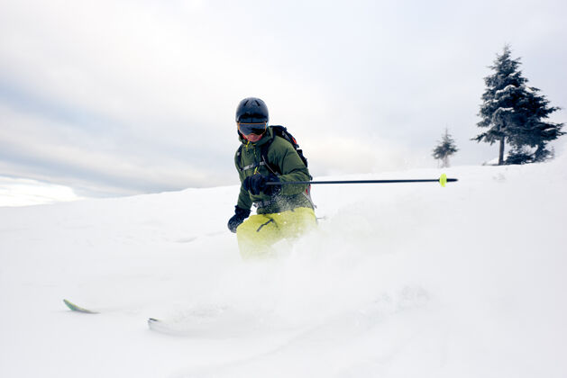 高滑雪者在雪山上穿着深粉滑雪者极限滑雪概念灰色的天空和松树的背景前视图男边缘头盔
