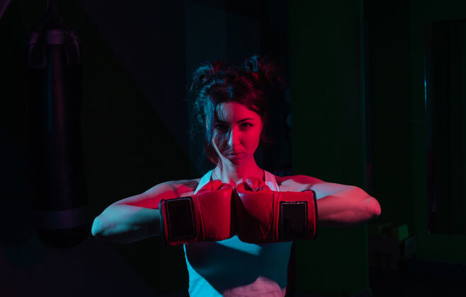 手套年轻女子拳击手戴着拳击手套 在霓虹灯的渐变红蓝色灯光下 在黑暗的墙上拳击运动员跆拳道