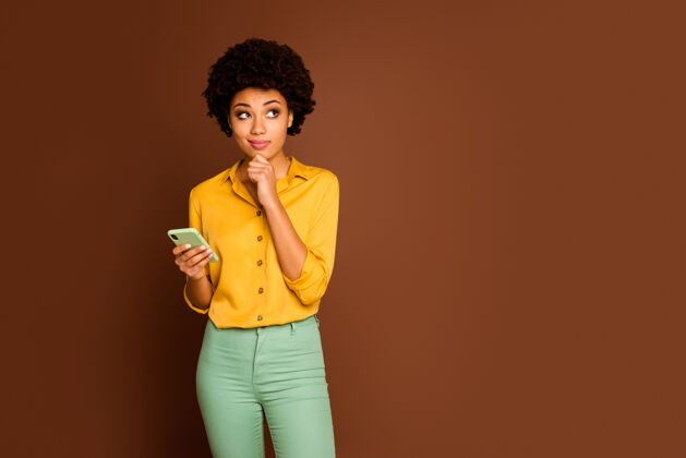 多民族有创意的非裔美国女孩用手机写真想发帖评论想梦幻的样子复制空间摸下巴手穿黄绿色裤子隔离棕色头发女孩女人