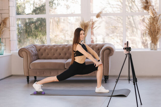 室内年轻的女运动员博主在balcksportswear拍摄视频 因为她在家里客厅锻炼电话护理瑜伽